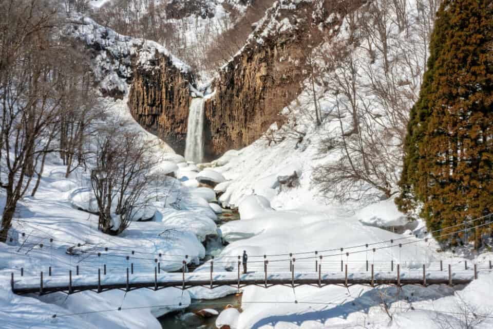 Naena waterfall in winter surrounded by deep snow. A person standing on the bridge in-front of the waterfall.